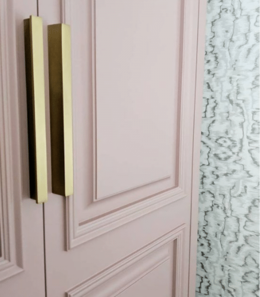 Blush pink classic wood door with decorative applied moulding and brass handles.