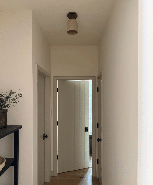 Minimalist hallway with white interior transitional wood door, black hardware, and natural wood flooring